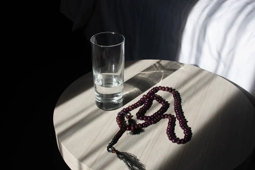 a beaded necklace sitting on a table next to a glass of water